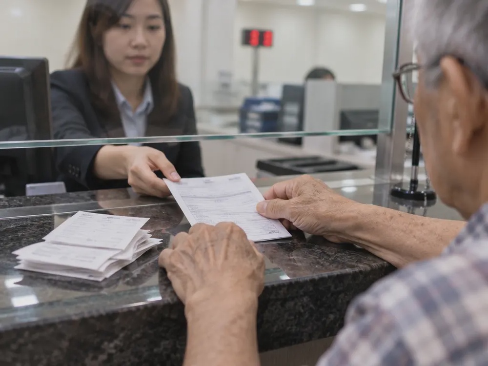 长者在金融机构柜台递交转账单据，旁边叠着多张收据的示意图