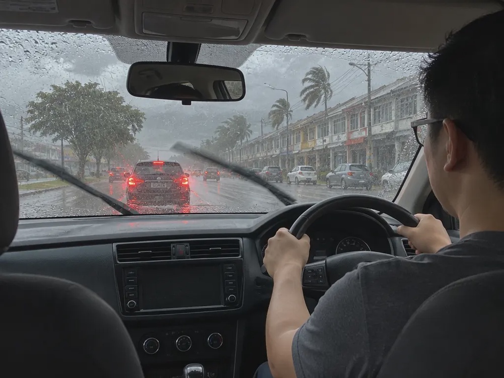 示意图：大雨中司机双手握方向盘慢驾，雨刷刮着挡风玻璃