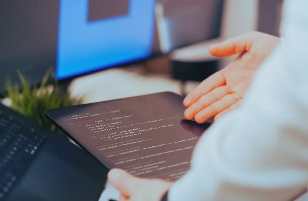 Developer reviewing code on tablet with laptop setup, representing modern app development and software engineering workflow.