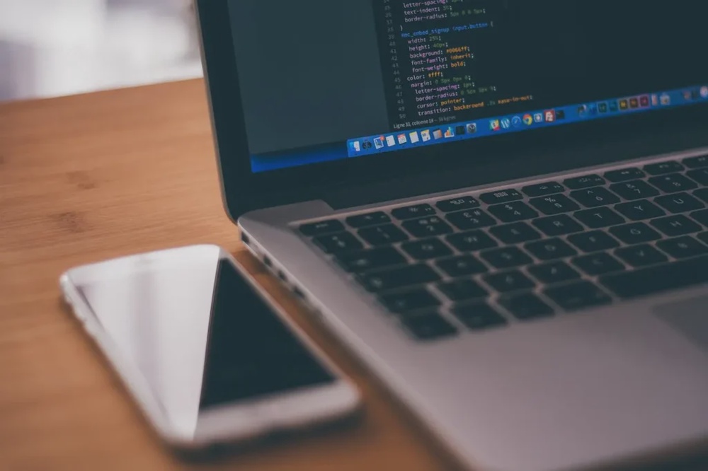 Laptop with code and mobile device, representing web application development and cross-device software solutions.