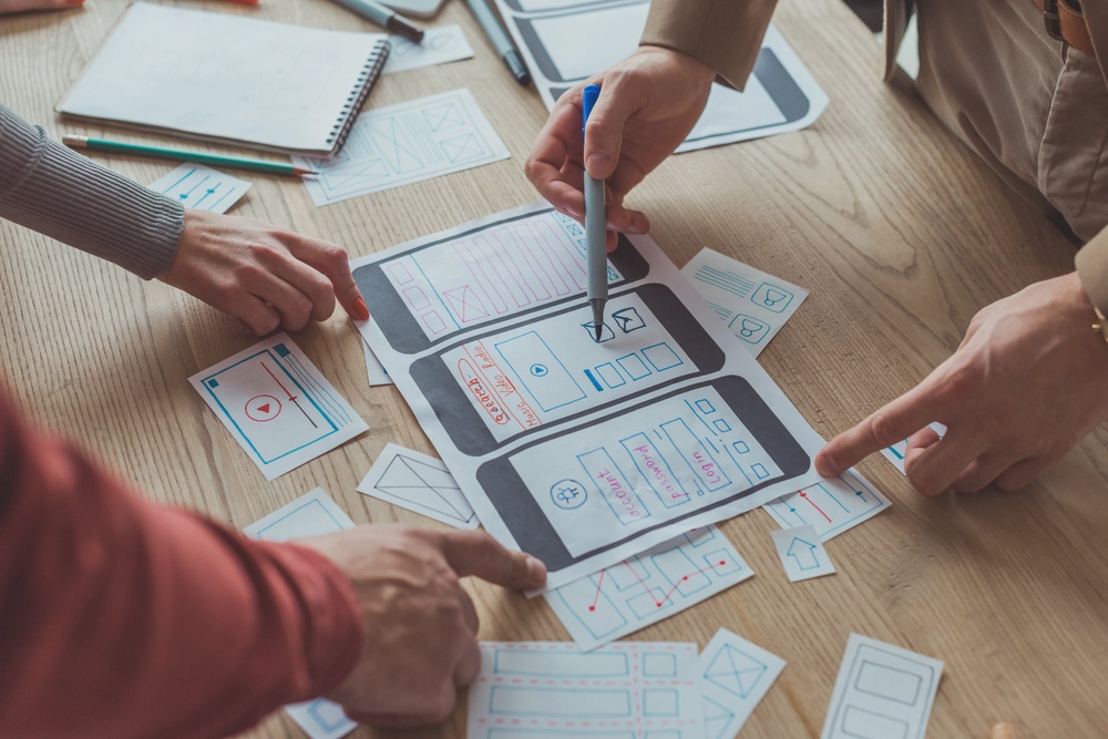 Two pair of hands arranging papers to arrange an app user journey, represnting the app development method.