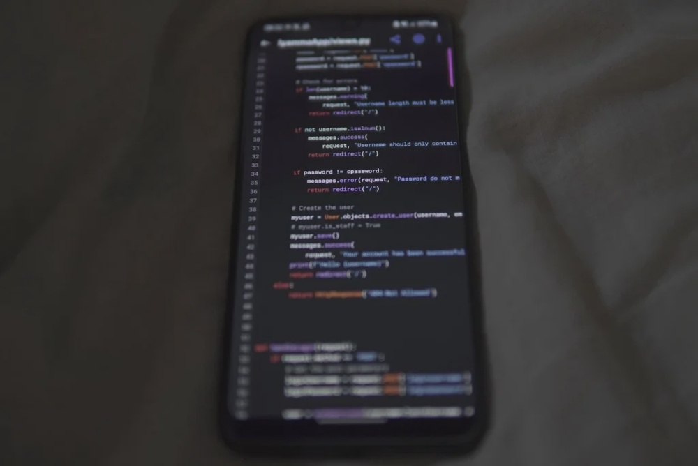Smartphone displaying programming code on a dark screen, placed on grey fabric.