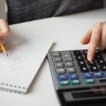 Person using a calculator and writing financial calculations in a notebook for budgeting, accounting, tax planning, or personal finance management.